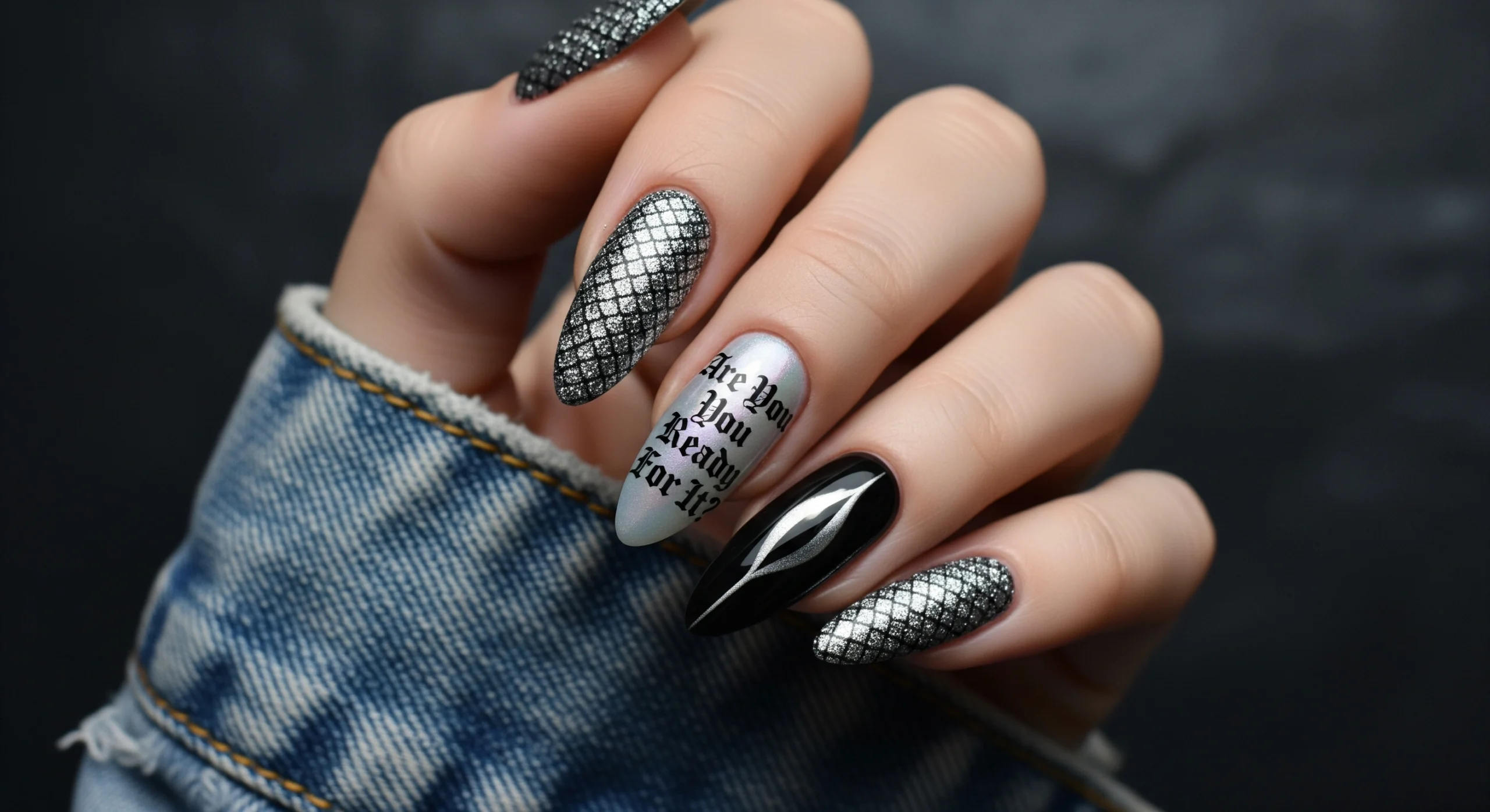 Close-up of almond-shaped nails inspired by Taylor Swift's Reputation album, featuring gunmetal grey snake skin texture, black and silver cat-eye polish, and a nail decal with Gothic text reading "Are You Ready For It?"